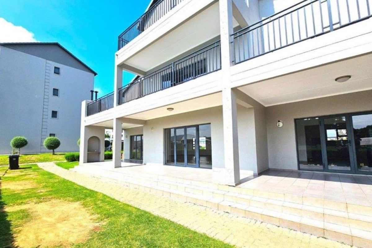 Rear view of a modern apartment building featuring a spacious tiled patio, upper-level balconies with metal railings, and large sliding glass doors.