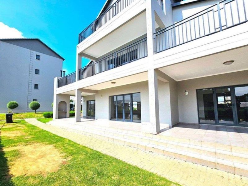 Rear view of a modern apartment building featuring a spacious tiled patio, upper-level balconies with metal railings, and large sliding glass doors.