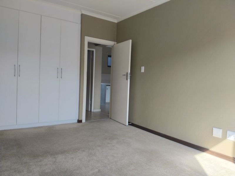 A clean, empty bedroom featuring neutral wall tones, carpeted flooring, and ample built-in cupboard storage space.