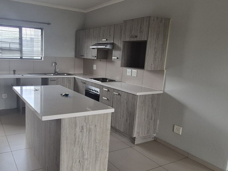 Modern kitchen featuring light wood-grain cabinetry, stone countertops, a central island, and built-in appliances, offering a clean and functional workspace.
