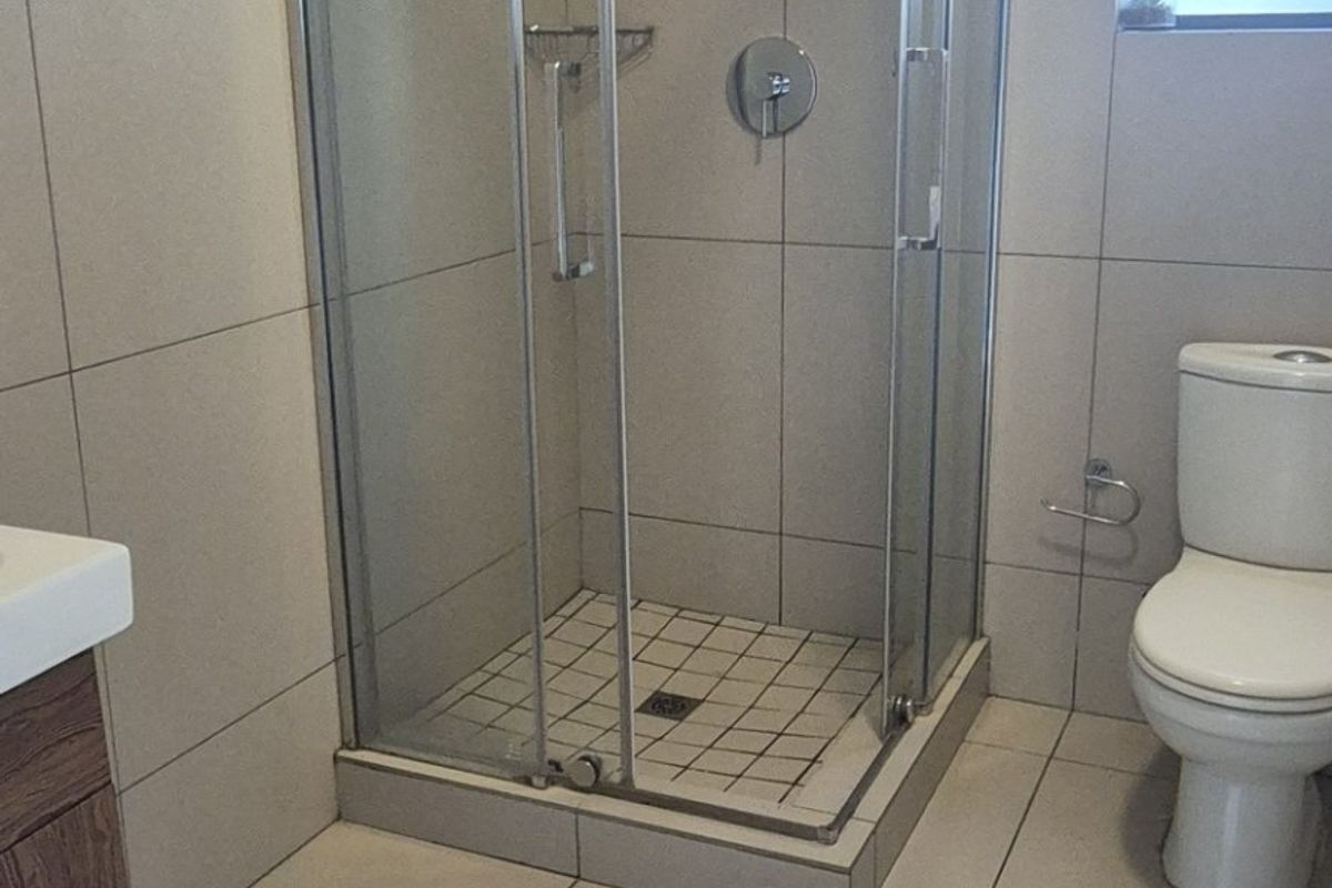 A clean, modern bathroom featuring a glass-enclosed shower, a vanity cabinet, and neutral floor-to-ceiling tiling.