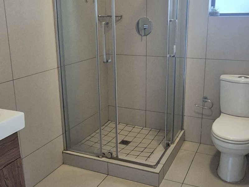 A clean, modern bathroom featuring a glass-enclosed shower, a vanity cabinet, and neutral floor-to-ceiling tiling.