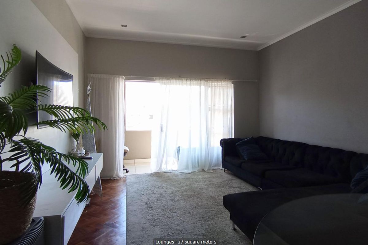 Spacious living room featuring warm parquet flooring, recessed lighting, and direct access to a private balcony through large sliding glass doors.
