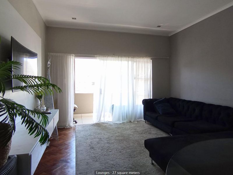 Spacious living room featuring warm parquet flooring, recessed lighting, and direct access to a private balcony through large sliding glass doors.