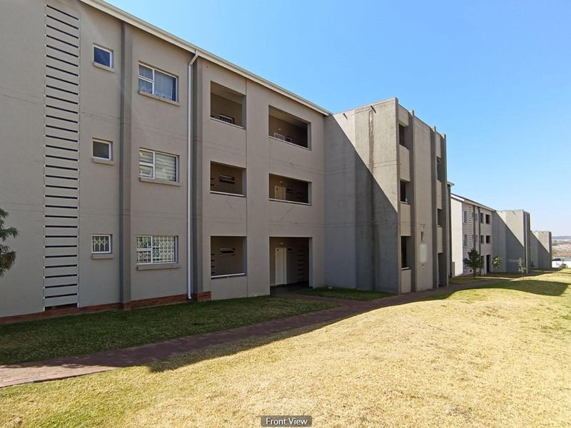 Exterior view of a multi-story apartment complex featuring a paved walkway, landscaped lawn, and private balconies.