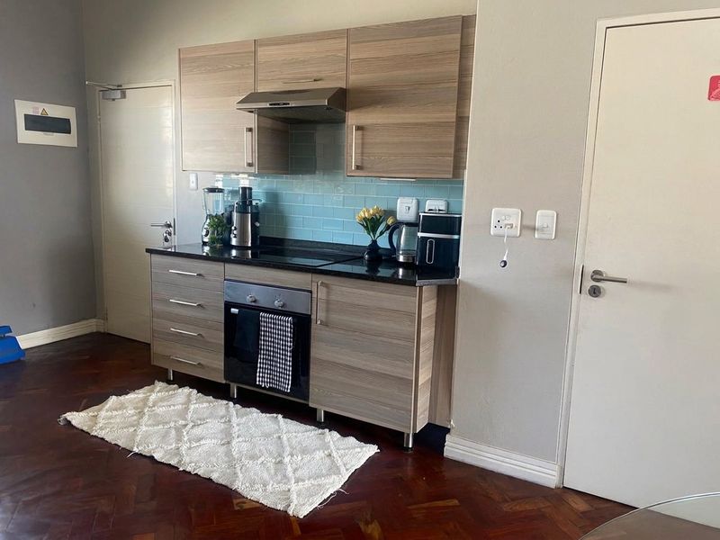 Compact modern kitchen featuring wood-finish cabinetry, dark countertops, a blue subway tile backsplash, and integrated appliances set against classic parquet flooring.