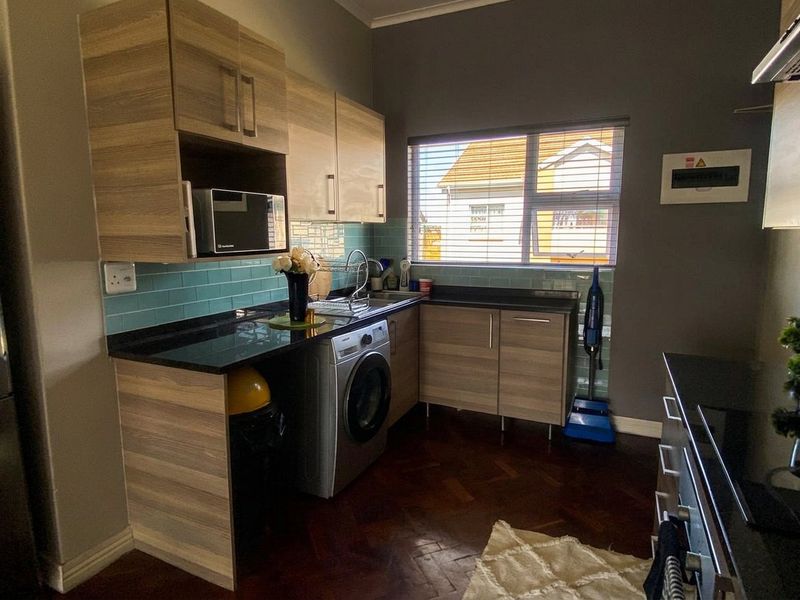A functional kitchen featuring wood-look laminate cabinetry, dark granite countertops, a teal subway tile backsplash, and classic parquet flooring.
