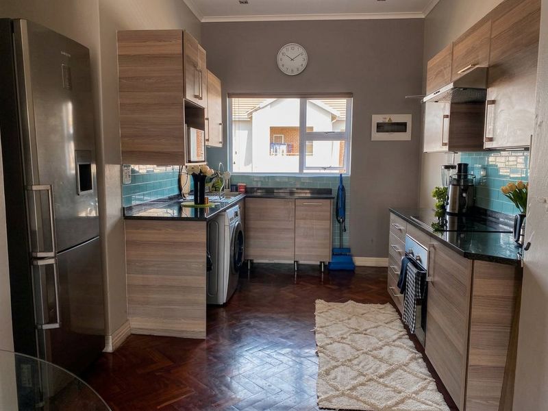 A functional kitchen featuring wood-finish cabinetry, granite countertops, a stylish teal subway tile backsplash, and classic parquet flooring.