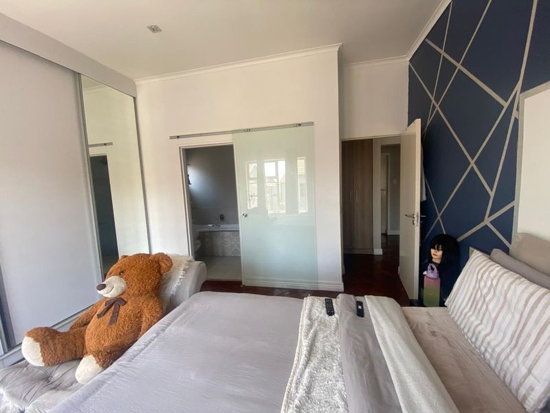 Spacious bedroom featuring parquet flooring, mirrored sliding wardrobes, and a modern frosted glass sliding door leading to an en-suite bathroom.