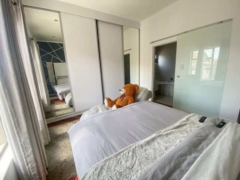 A well-maintained bedroom featuring extensive built-in mirrored wardrobes, hardwood flooring, and a modern sliding glass door leading to an en-suite bathroom.