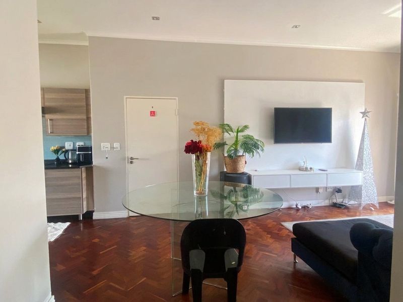 Open-plan living area featuring warm herringbone parquet flooring, a built-in media console, and an adjacent kitchen with modern cabinetry and tiled backsplash.