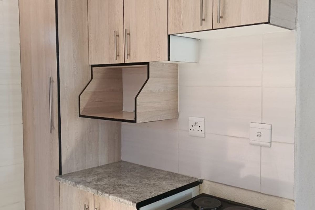 Compact kitchen featuring light wood-look cabinetry, tiled backsplash, and a freestanding electric stove with oven.