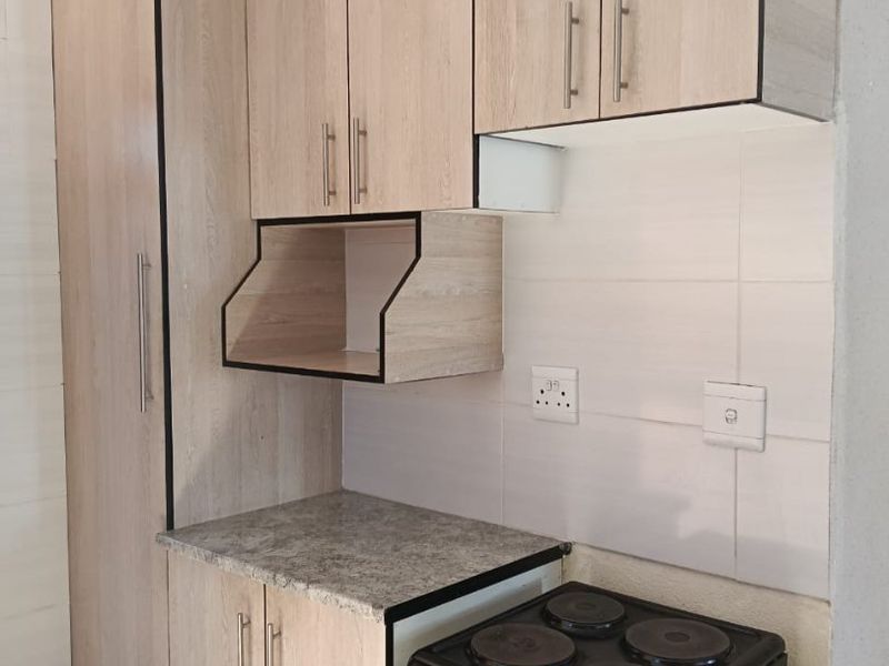 Compact kitchen featuring light wood-look cabinetry, tiled backsplash, and a freestanding electric stove with oven.