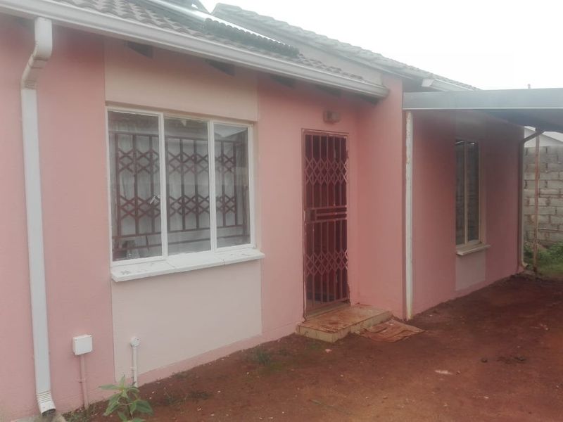Front exterior view of a single-story house featuring a pink facade, security gates, and an attached carport area.