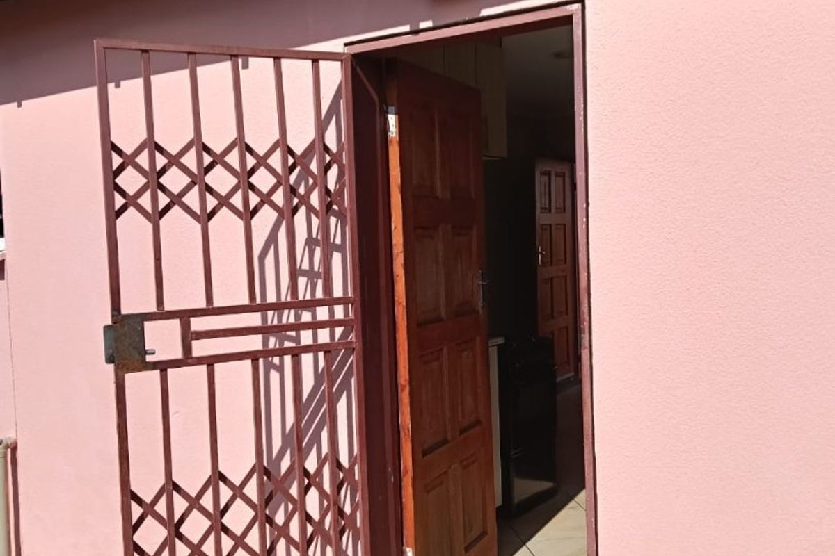 Rear exterior view of the property featuring a security gate, timber door, and external lighting.