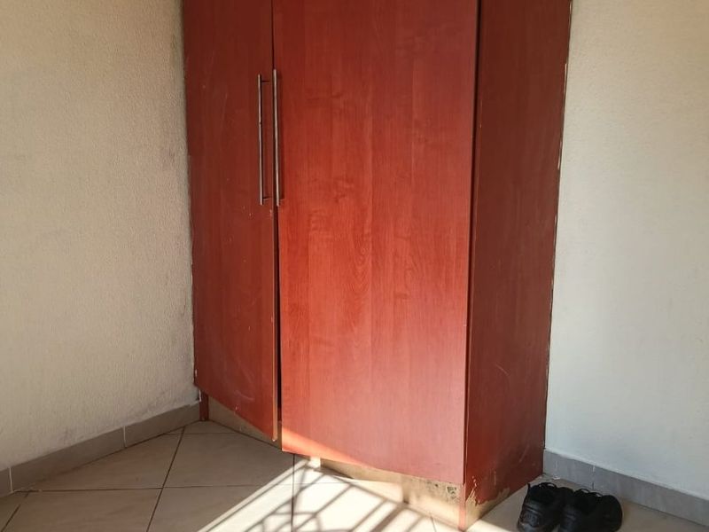 A bedroom corner featuring a built-in wooden wardrobe and tiled flooring, showing signs of wear and tear.