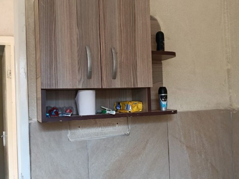 A bathroom wall featuring a wood-look vanity cabinet mounted above partially tiled walls with visible unfinished plasterwork.