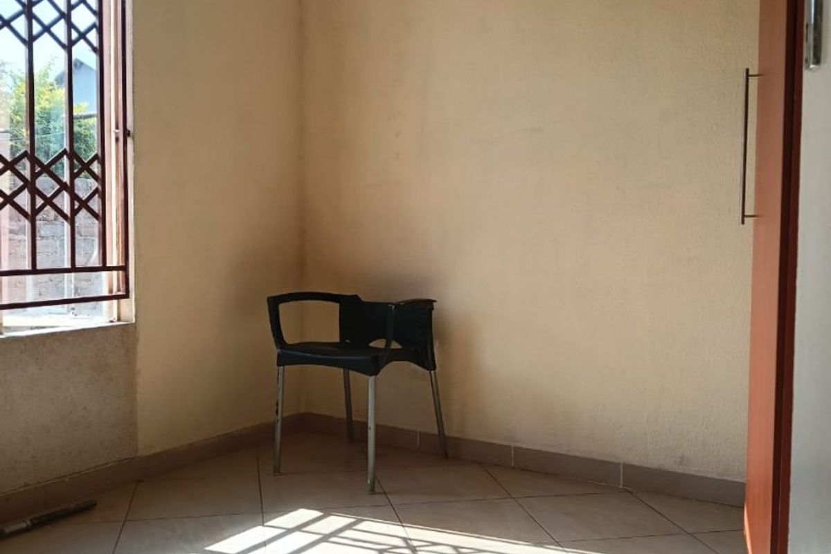 A vacant bedroom featuring tiled flooring and a window fitted with a security gate, offering a blank canvas for potential interior design updates.