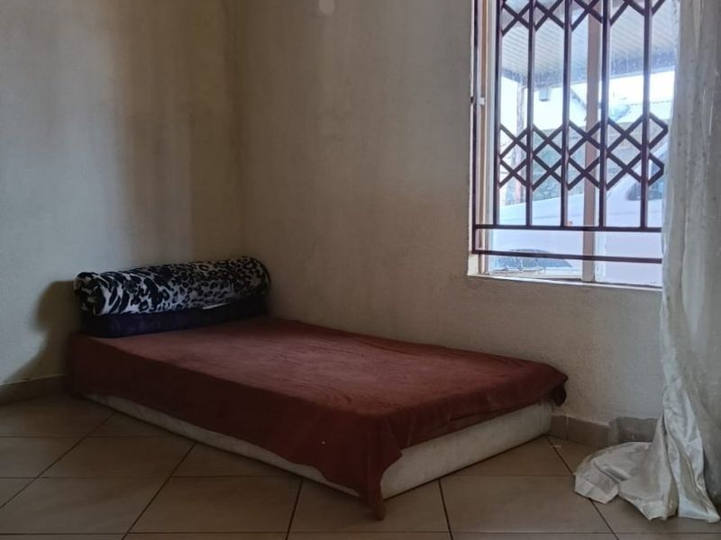 A bedroom featuring tiled flooring and a window fitted with a security gate, requiring cosmetic wall repairs and fresh paint.