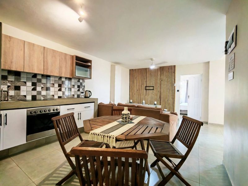 Open-plan living area featuring a modern kitchen with built-in cabinetry, electric oven, hob, and a decorative timber slat feature wall.