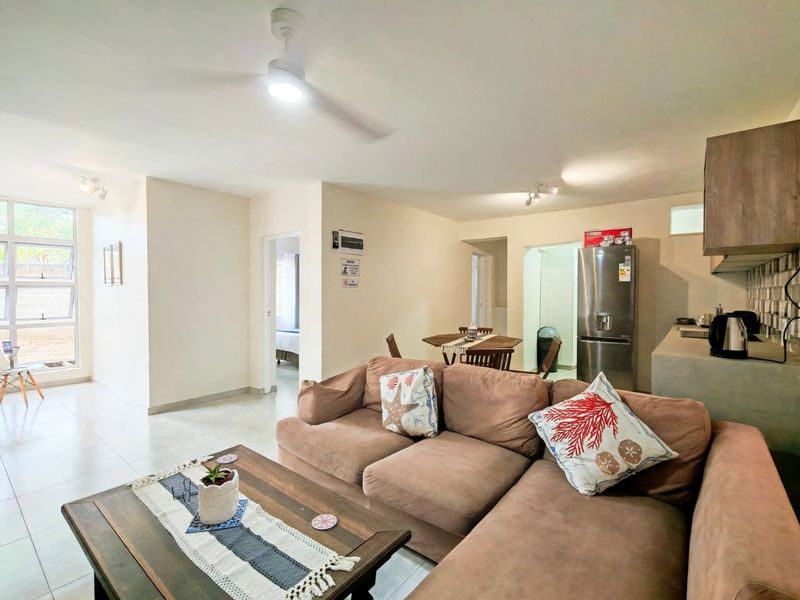 Open-plan living and kitchen area featuring tiled flooring, a ceiling fan, and functional built-in cabinetry with a tiled backsplash.
