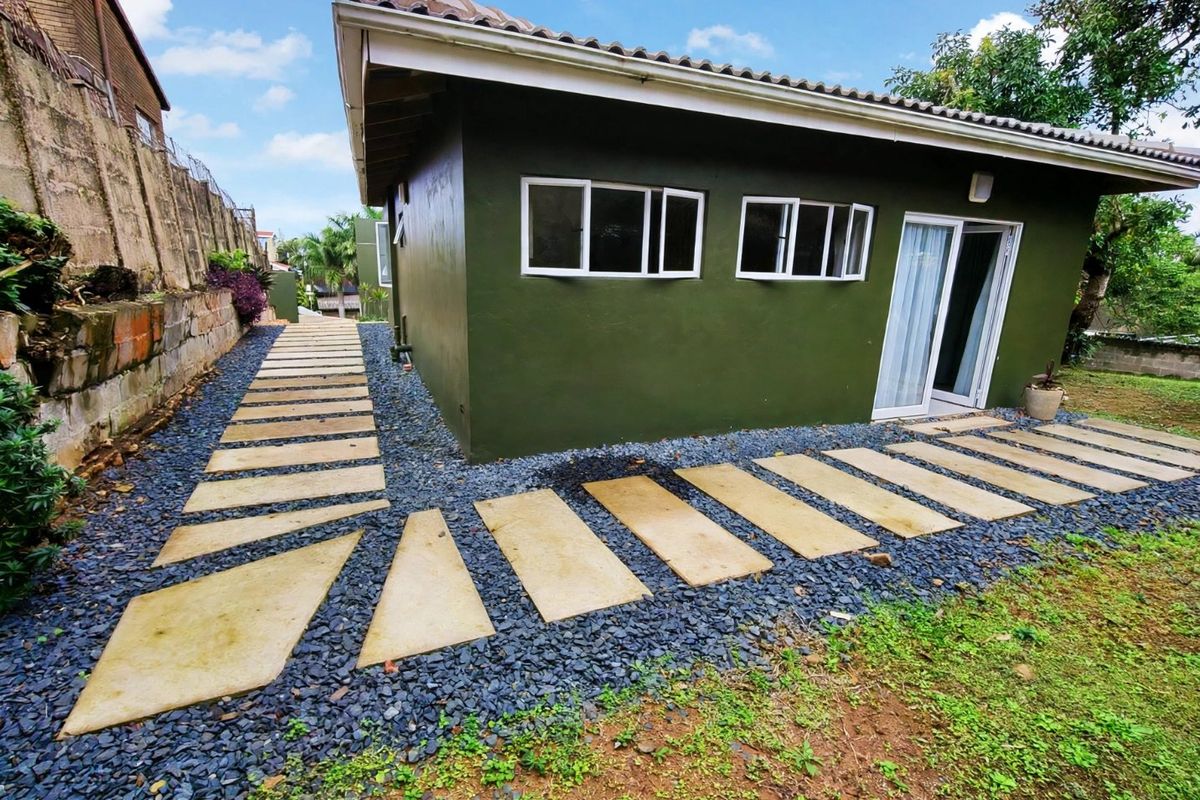 Rear view of the property featuring a paved walkway, gravel landscaping, and a sliding glass door entrance.