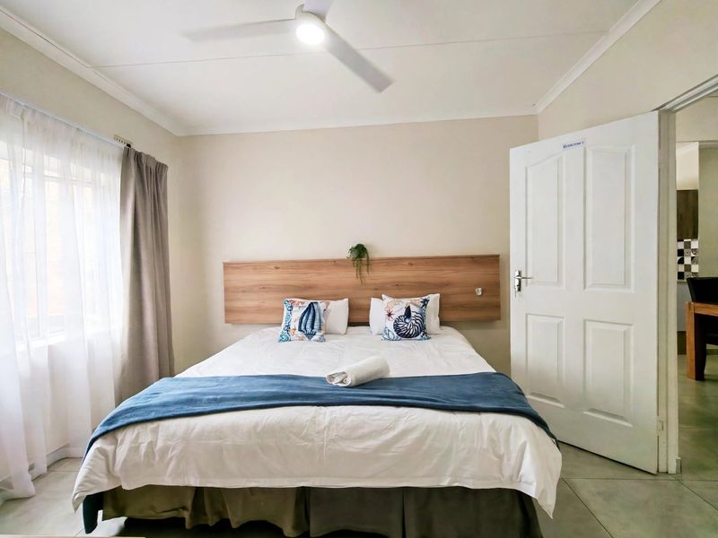 A well-maintained bedroom featuring a built-in wooden headboard, ceiling fan, and neutral tiled flooring, offering a clean and functional living space.