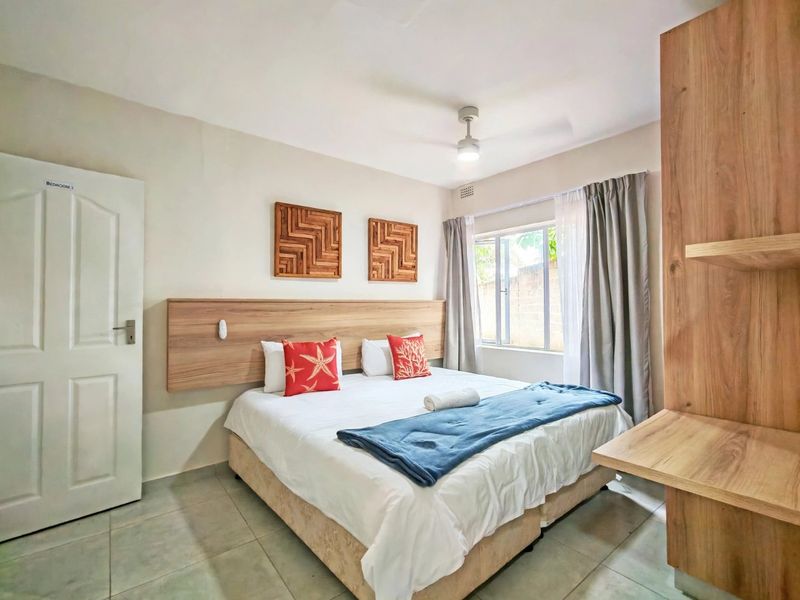 A well-maintained bedroom featuring a built-in wooden headboard, ceiling fan, and neutral tiled flooring, offering a clean and functional living space.