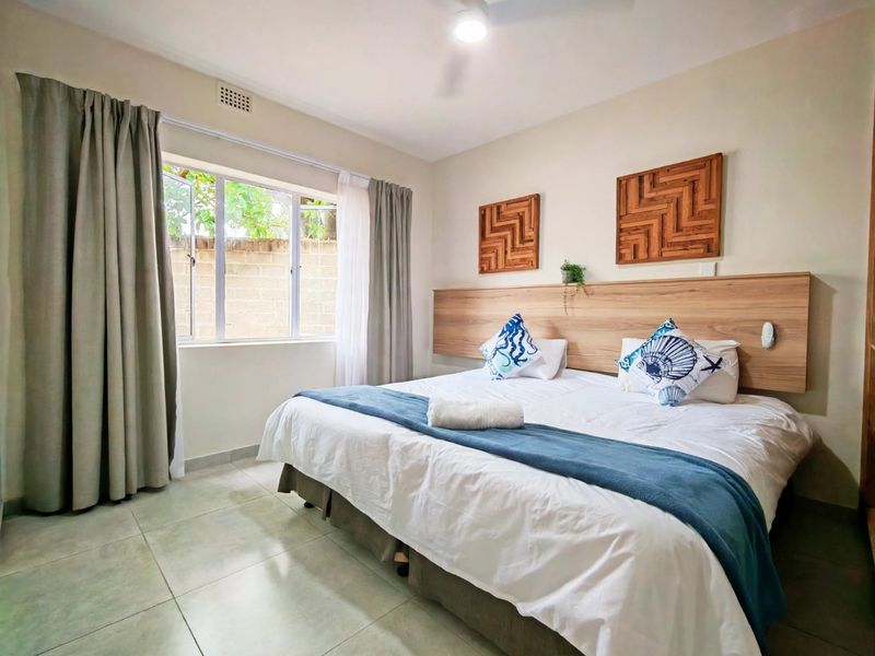 A well-maintained bedroom featuring tiled flooring, a built-in wooden headboard, and a ceiling fan, providing a comfortable and functional sleeping space.