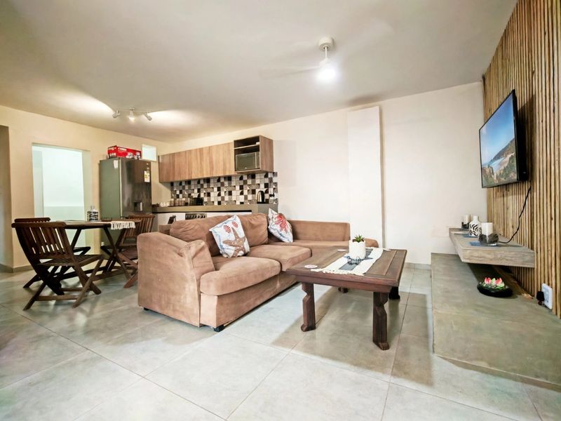 Open-plan living area featuring tiled floors, a modern slatted wood feature wall, built-in media console, and a functional kitchen with wood-tone cabinetry.