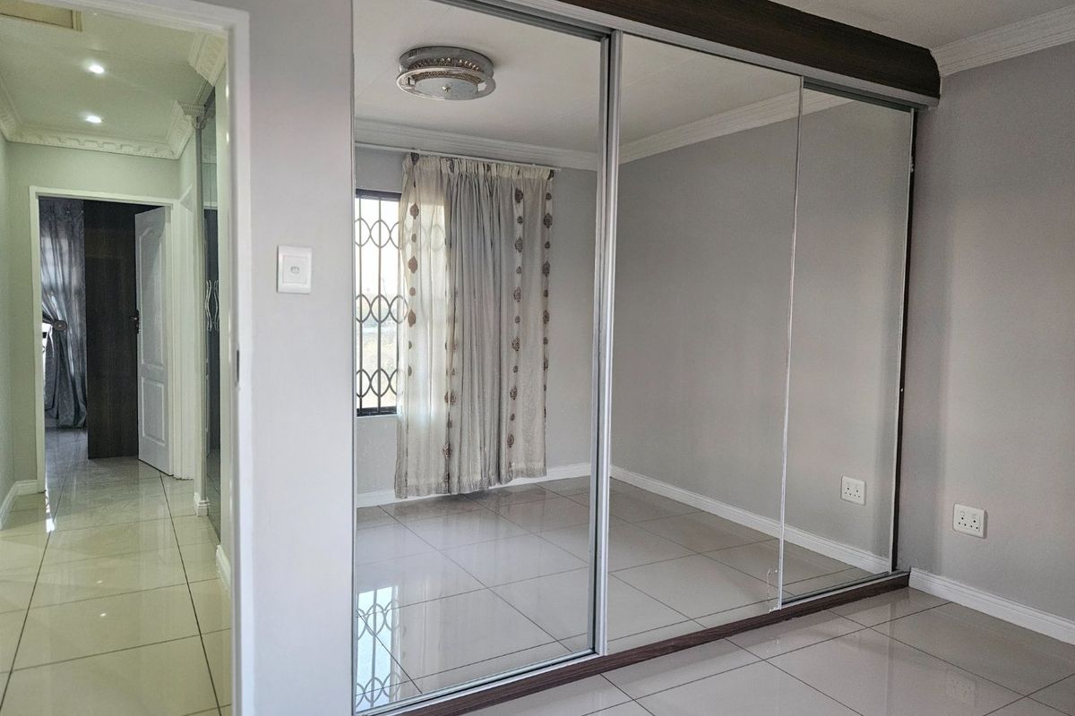 A bright, empty bedroom featuring large built-in mirrored sliding wardrobes, neutral tiled flooring, and classic ceiling cornicing.
