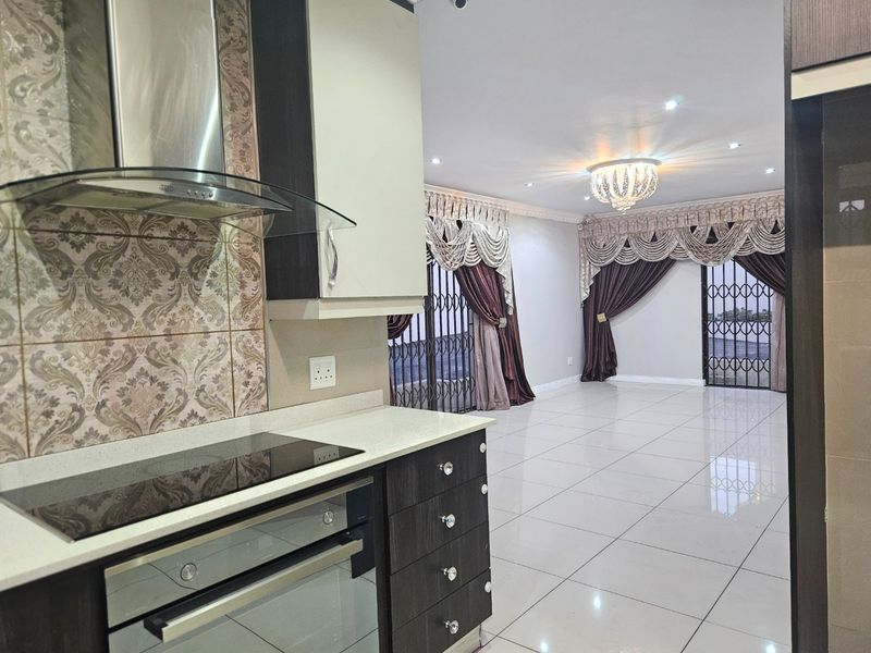 Open-plan kitchen and living area featuring modern cabinetry, built-in appliances, tiled flooring, and security gates leading to the exterior.