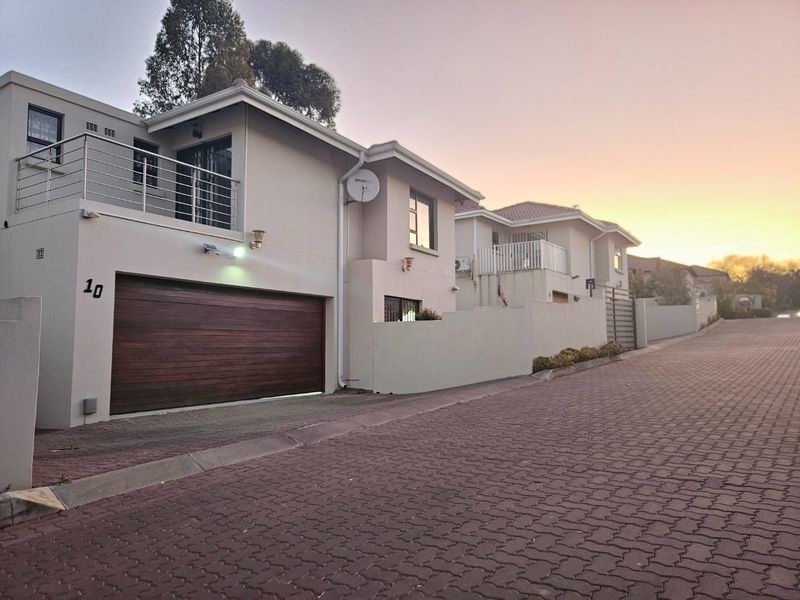 Front exterior view of a modern townhouse featuring a timber garage door, paved driveway, and an upper-level balcony with stainless steel railings.