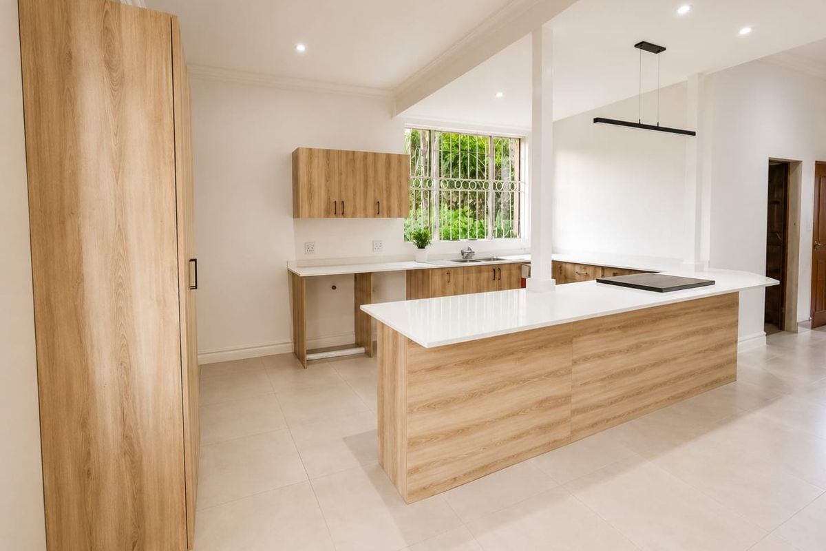 Modern, renovated kitchen featuring light wood-grain cabinetry, stone countertops, a central island with a cooktop, and ample natural light.