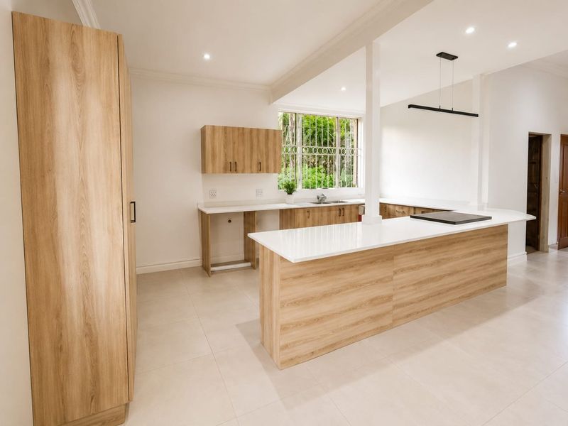 Modern, renovated kitchen featuring light wood-grain cabinetry, stone countertops, a central island with a cooktop, and ample natural light.
