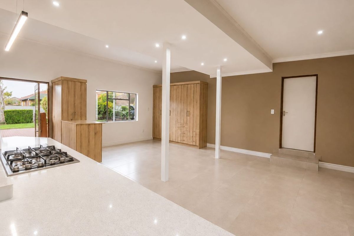 Spacious open-plan living area featuring a modern kitchen with stone countertops, gas hob, built-in cabinetry, and neutral tiled flooring throughout.