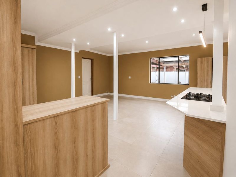 Spacious open-plan living area featuring modern wood-finish cabinetry, stone countertops, a built-in gas hob, and neutral tiled flooring throughout.