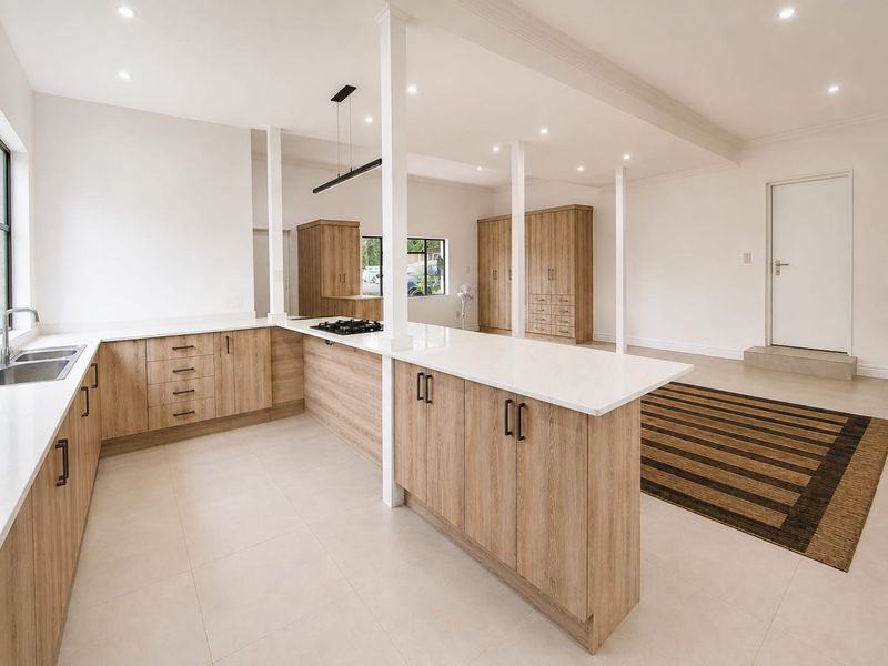 Modern open-plan kitchen featuring light wood cabinetry, stone countertops, a gas hob, and integrated storage, finished with neutral floor tiles and recessed lighting.