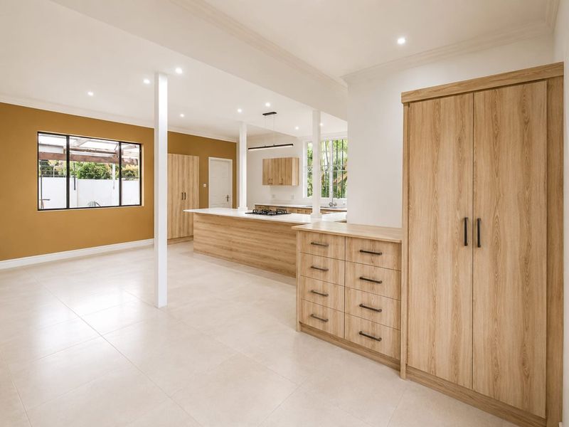 Spacious open-plan living and kitchen area featuring modern light wood cabinetry, a central island with a gas hob, and neutral tiled flooring.