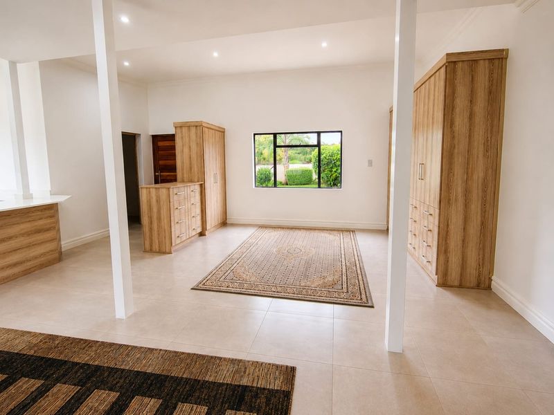 Spacious open-plan living area featuring neutral tiled flooring, built-in wooden cabinetry, and recessed lighting, offering a bright and versatile layout.
