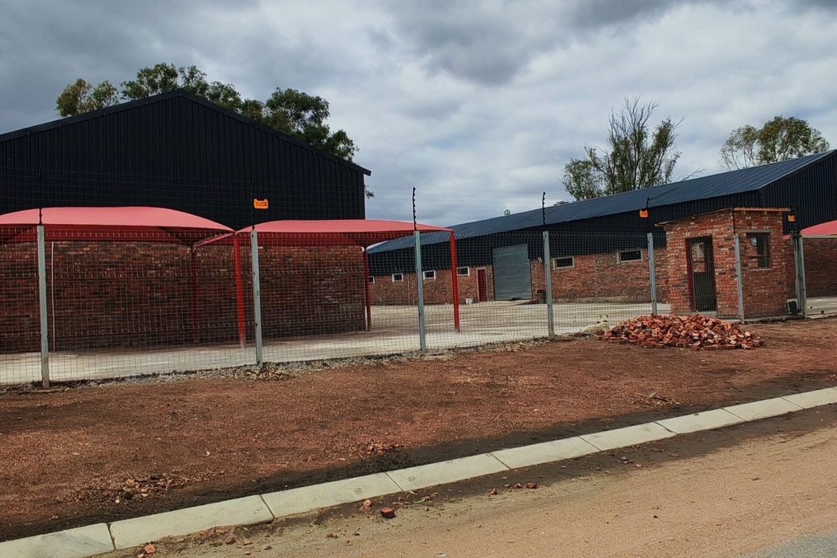 Industrial property featuring multiple warehouse structures, shade ports, security fencing, and a dedicated guard house on a paved and unpaved site.