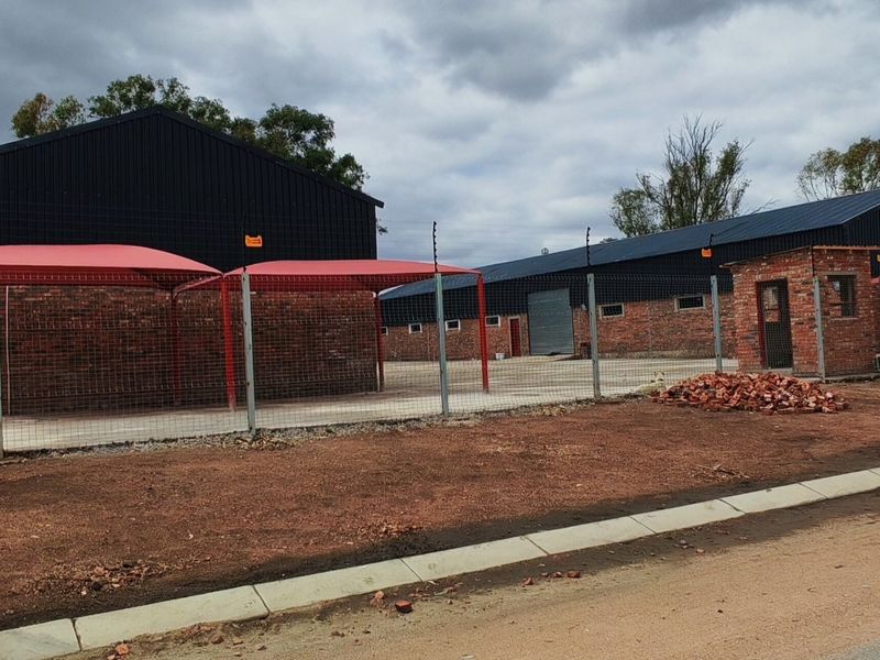 Industrial property featuring multiple warehouse structures, shade ports, security fencing, and a dedicated guard house on a paved and unpaved site.