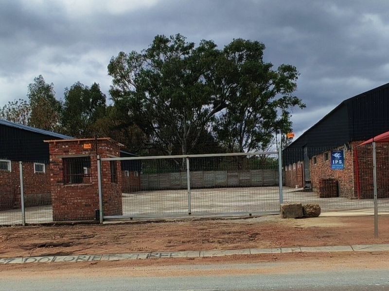 Industrial property featuring a secure gated entrance, brick gatehouse, expansive concrete yard, and multiple shade cloth parking bays.