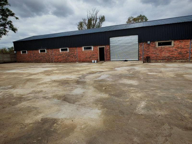 Industrial property featuring a large concrete yard, brick facade, and a secure roller shutter door access point.