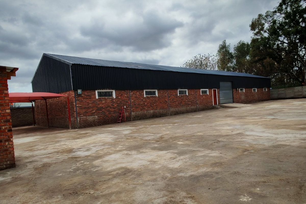 Industrial warehouse building featuring a brick facade, metal roofing, a roller shutter door, and a large concrete yard area.