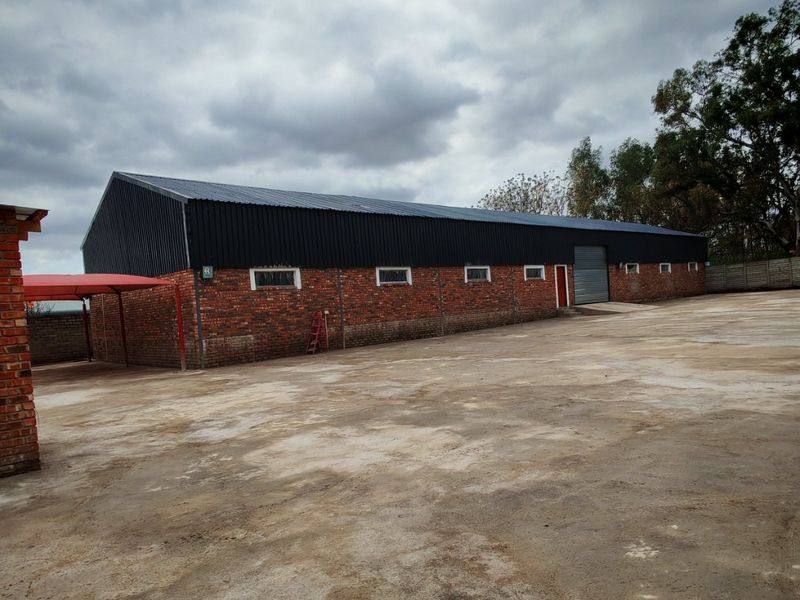 Industrial warehouse building featuring a brick facade, metal roofing, a roller shutter door, and a large concrete yard area.