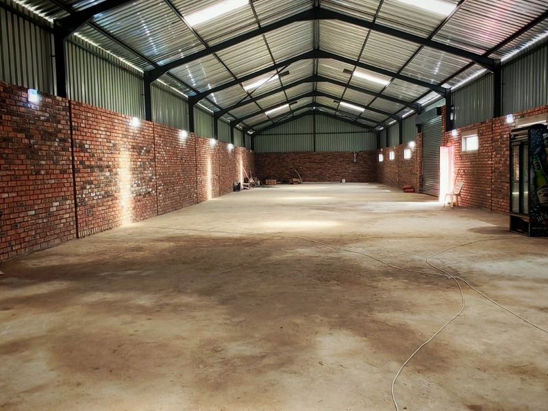 Spacious industrial warehouse unit featuring exposed brick walls, high-clearance corrugated metal roofing with integrated skylights, and durable concrete flooring.
