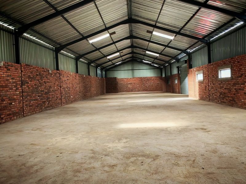 Spacious industrial warehouse unit featuring exposed brick walls, a high-clearance steel portal frame, concrete flooring, and natural light through roof skylights.