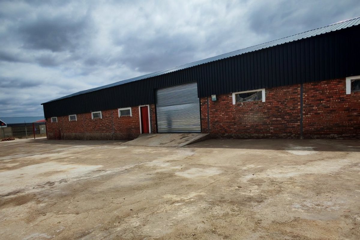 Industrial warehouse exterior featuring a large roller shutter door, loading ramp, and expansive concrete yard area.