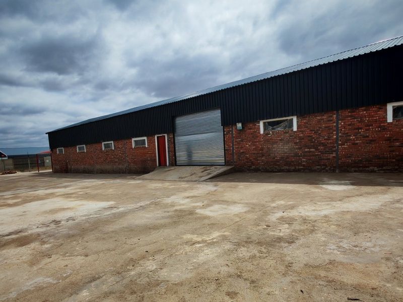 Industrial warehouse exterior featuring a large roller shutter door, loading ramp, and expansive concrete yard area.